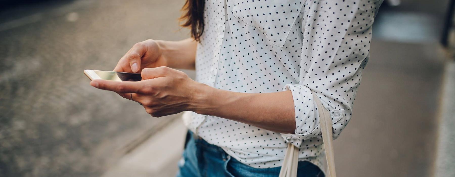 woman walks down the street and texts with a bag of groceries on her arm